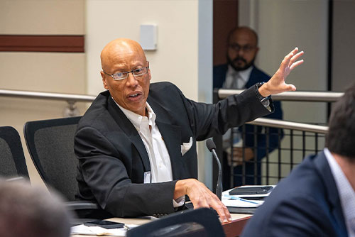 A seated audience member raises his hand to ask a question during the 2023 Chicago Payments Symposium.